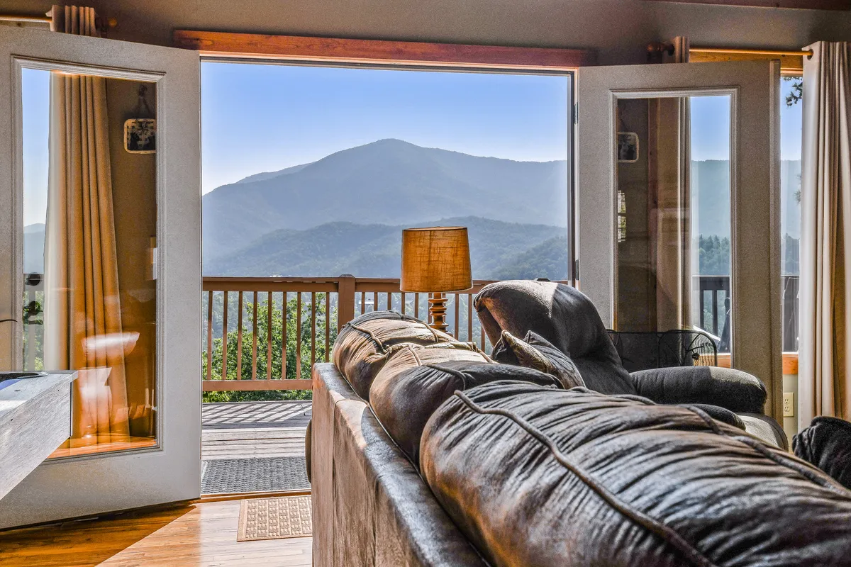 A cozy sofa is positioned by expansive windows that reveal a breathtaking mountain view. Soft lighting from a nearby lamp and an inviting atmosphere make this spot ideal for relaxing with a book or hosting friends.