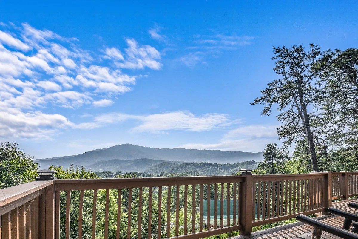 A breathtaking mountain view unfolds from a wooden deck, with clouds drifting over the treetops and tranquil surroundings ideal for sunrise vistas, stargazing, or peaceful reading.