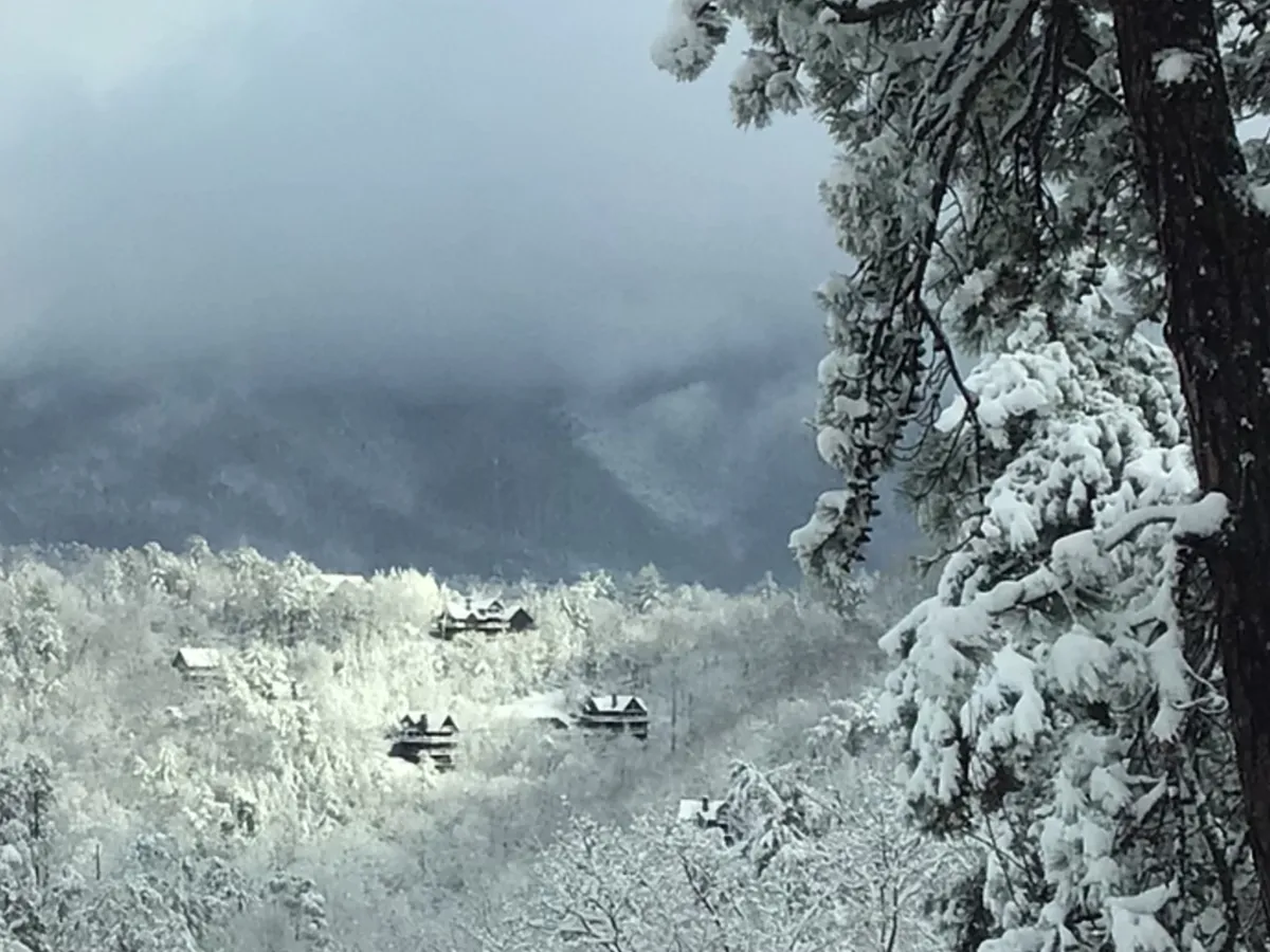 A sweeping view of snow-covered mountains, dotted with distant cabins and pine trees, under a tranquil sky. The scene suggests immersion in natural beauty and year-round possibilities for adventure and relaxation.