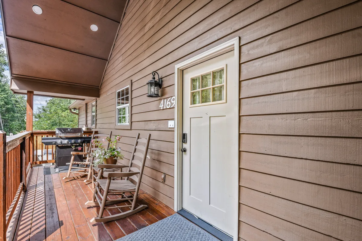 An inviting shot of the front porch, complete with rocking chairs, flowers in a planter, and a lantern-style light fixture. The entrance is easily visible, suggesting step-free access and a warm welcome for guests of all ages.