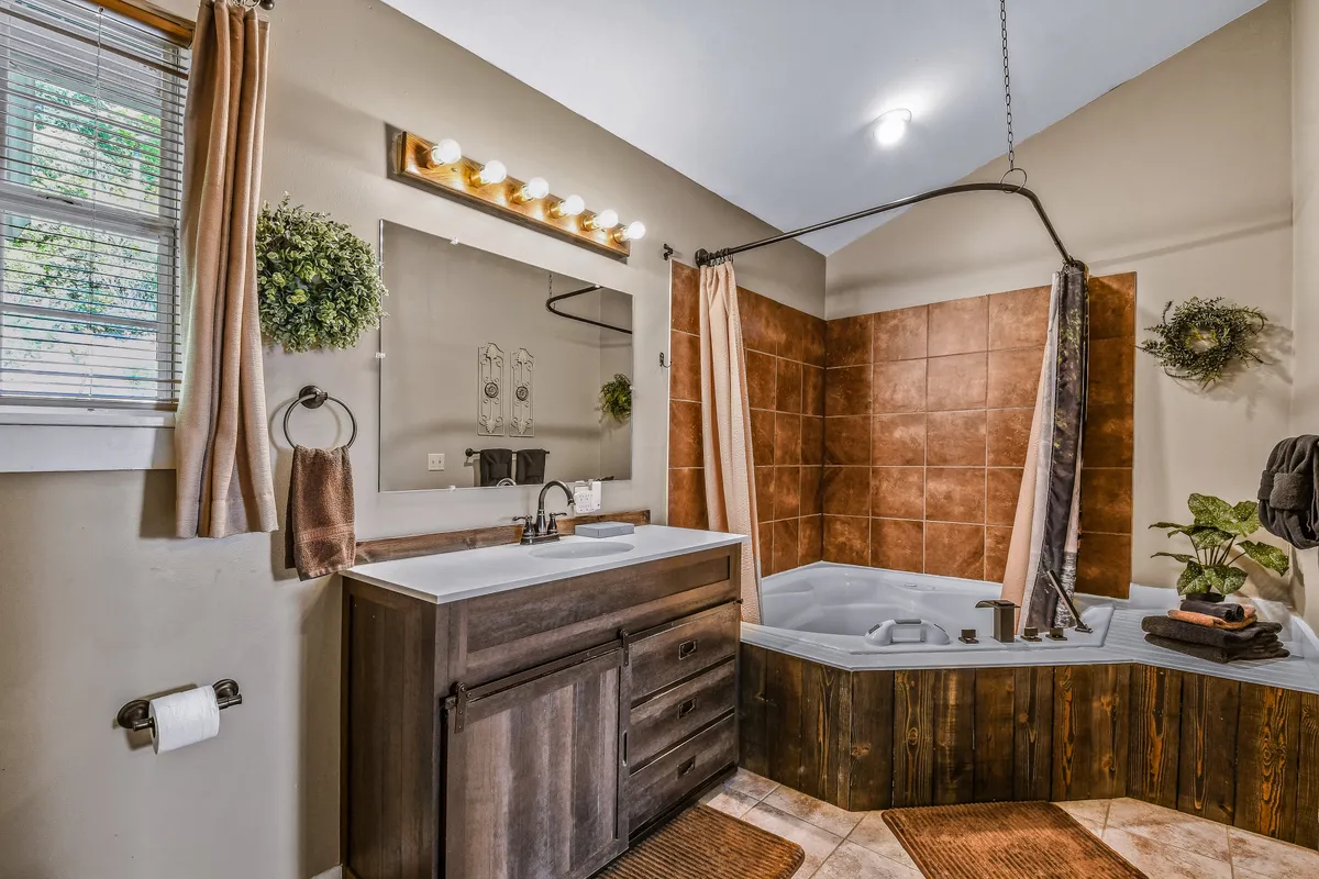 A serene bathroom scene with a vanity and sink, jacuzzi (jetted) tub, a large mirror, and decorative plants. The lighting is soft and the setup suggests a peaceful, spa-like experience.