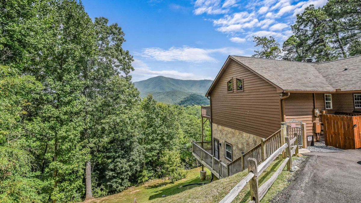 A peaceful deck overlooking a stunning mountain view, bordered by lush trees. The scene suggests opportunities for outdoor relaxation, social gatherings, and easy connection to nature, all just steps from the main living area.