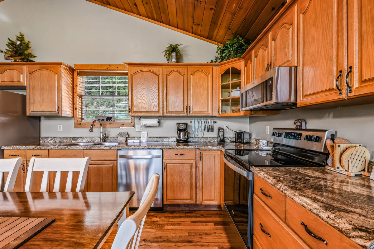 A welcoming open-concept kitchen and dining area featuring sleek granite countertops, warm wooden cabinets, and modern stainless steel appliances. The spacious dining table is set nearby, ideal for family gatherings or group meals.